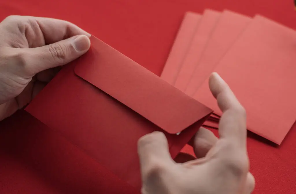 Mise sous plis à Domicile, un vrai métier rentable ? 1 Une main tient une enveloppe rouge sur une table.
