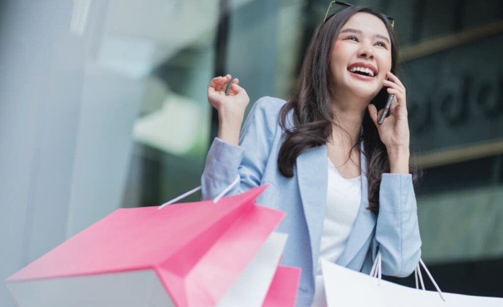 Femme asiatique tenant des sacs à provisions tout en parlant au téléphone.