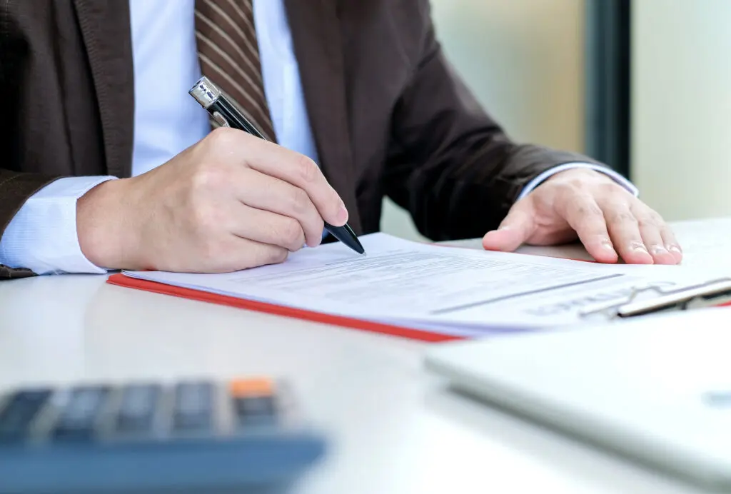 Comment remplir un chèque : Le guide ultra-complet pour éviter les erreurs 3 Un homme d'affaires signant un document au bureau tout en suivant un tutoriel étape par étape.