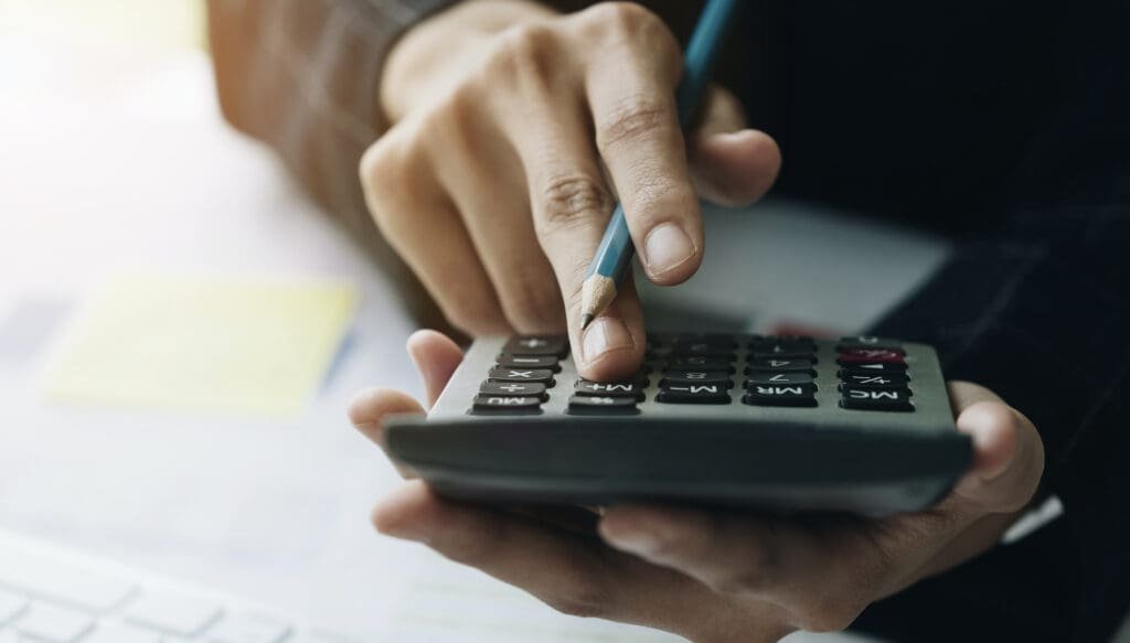 Une personne utilise une calculatrice sur un bureau pour remplir un chèque.