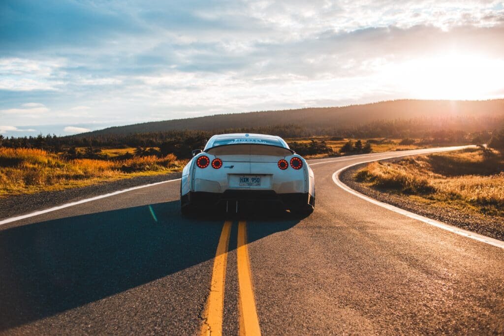 Une Nissan GTR blanche roulant sur une route au coucher du soleil.