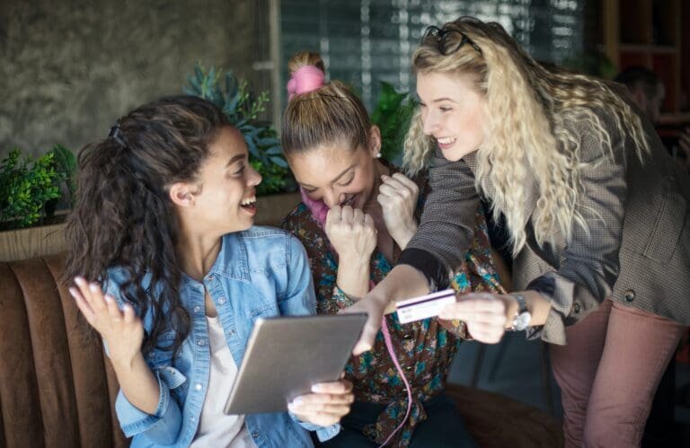 Trois femmes regardent une tablette alors qu'elles sont assises sur un canapé, parcourant une liste d'entreprises de vente de maisons.