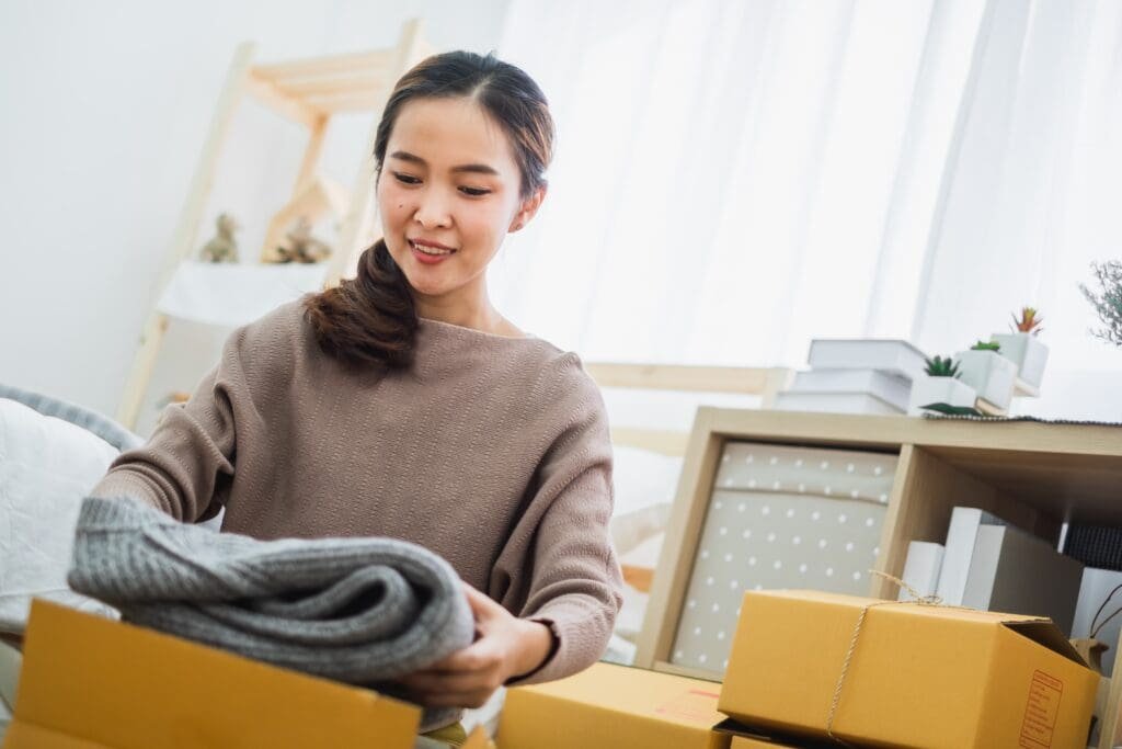 Femme asiatique ouvrant une boîte chez elle tout en maximisant ses profits grâce à Vinted.