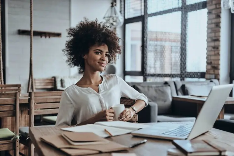 Une jeune femme assise à une table avec un ordinateur portable, trouvant l'inspiration dans 10 citations d'entrepreneurs qui vont changer sa vie.