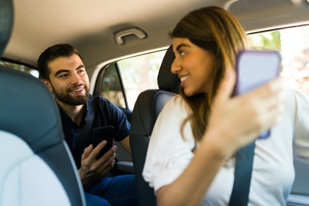 Un chauffeur Uber optimisant ses résultats en aidant un homme et une femme assis sur la banquette arrière de la voiture, absorbés par leurs téléphones portables.