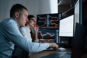 Deux personnes devant deux moniteurs avec des graphiques boursiers.