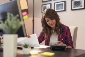 Une femme analysant et interprétant un état financier avec des papiers et une calculatrice.