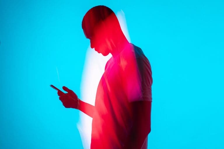 Voir une Story Instagram en Anonyme: les astuces 1 Un homme tenant un téléphone portable devant un fond bleu tout en regardant une histoire Instagram de manière anonyme.
