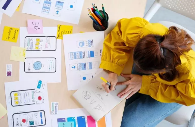 Web marketing : l'importance de votre charte graphique 1 Une femme est assise à une table avec des papiers dessus, discutant de l'importance du marketing Web et de votre conception graphique.