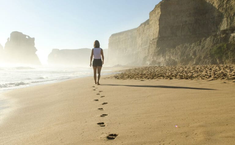 Une femme marchant sur une plage avec des empreintes dans le sable.