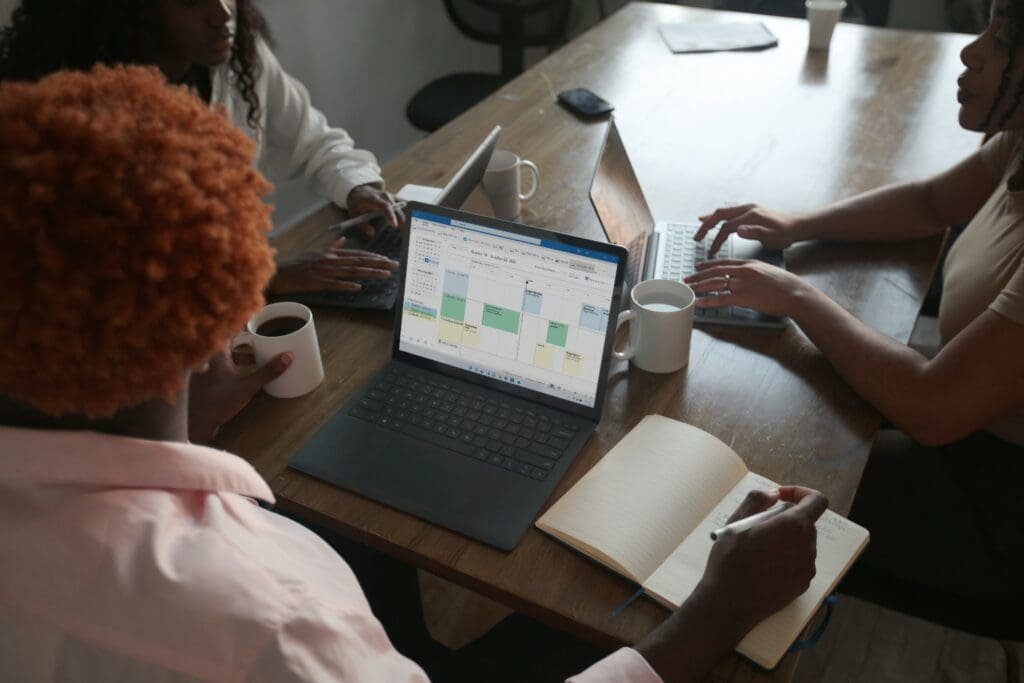 Un groupe de personnes assises autour d'une table avec des ordinateurs portables, connectant leurs appareils et participant à un didacticiel sur l'utilisation d'Excel et de Google Sheets.